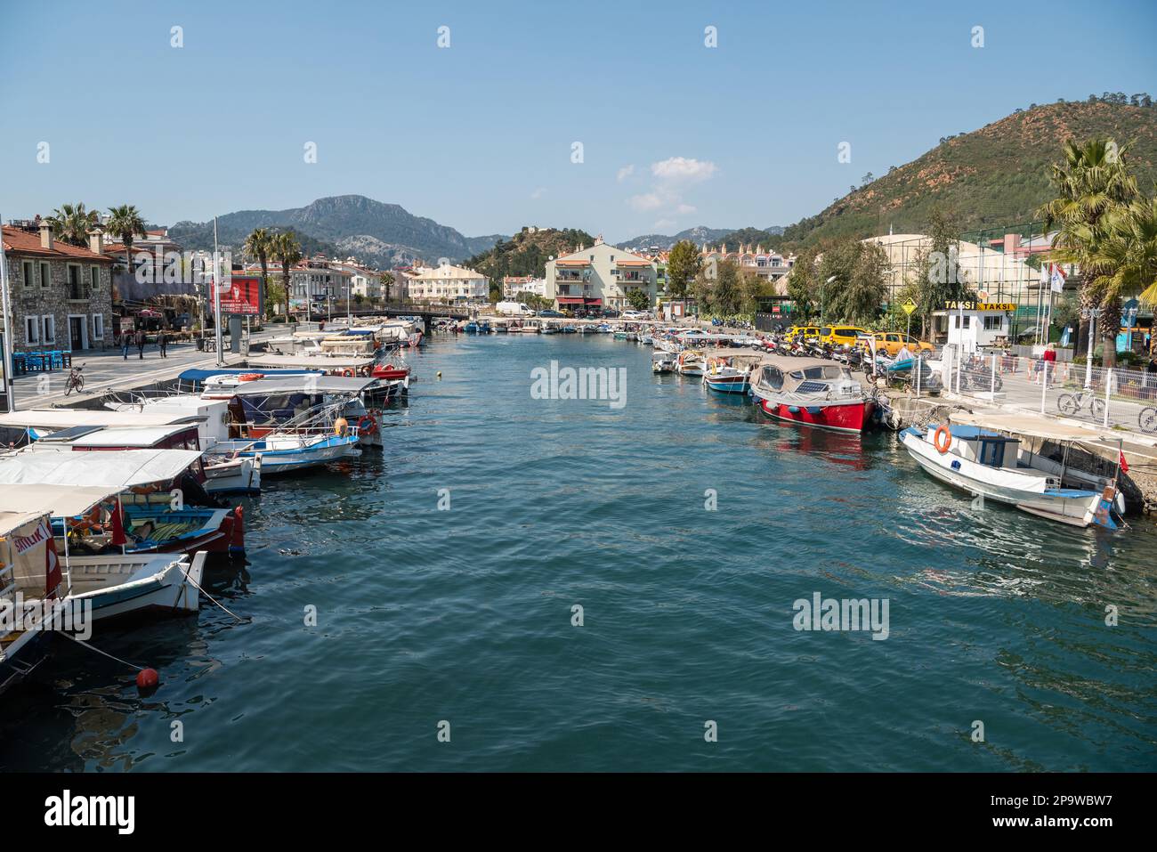 Marmaris, Turkey – March 25, 2022. Fishing boats municipal harbour in Marmaris, Turkey. View with boats, commercial properties and people. Stock Photo