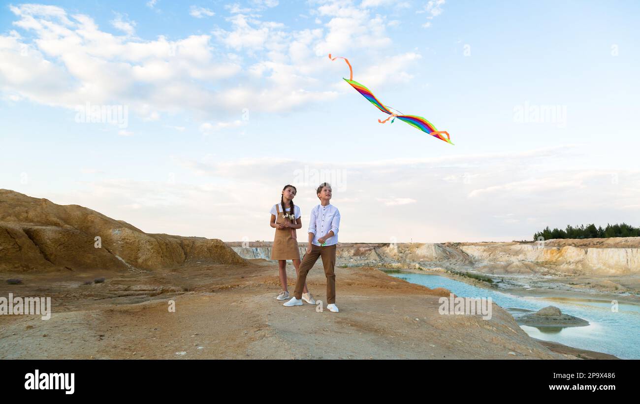 A boy and a girl launch a bright kite standing on the edge of a mountain near a pond. Stock Photo