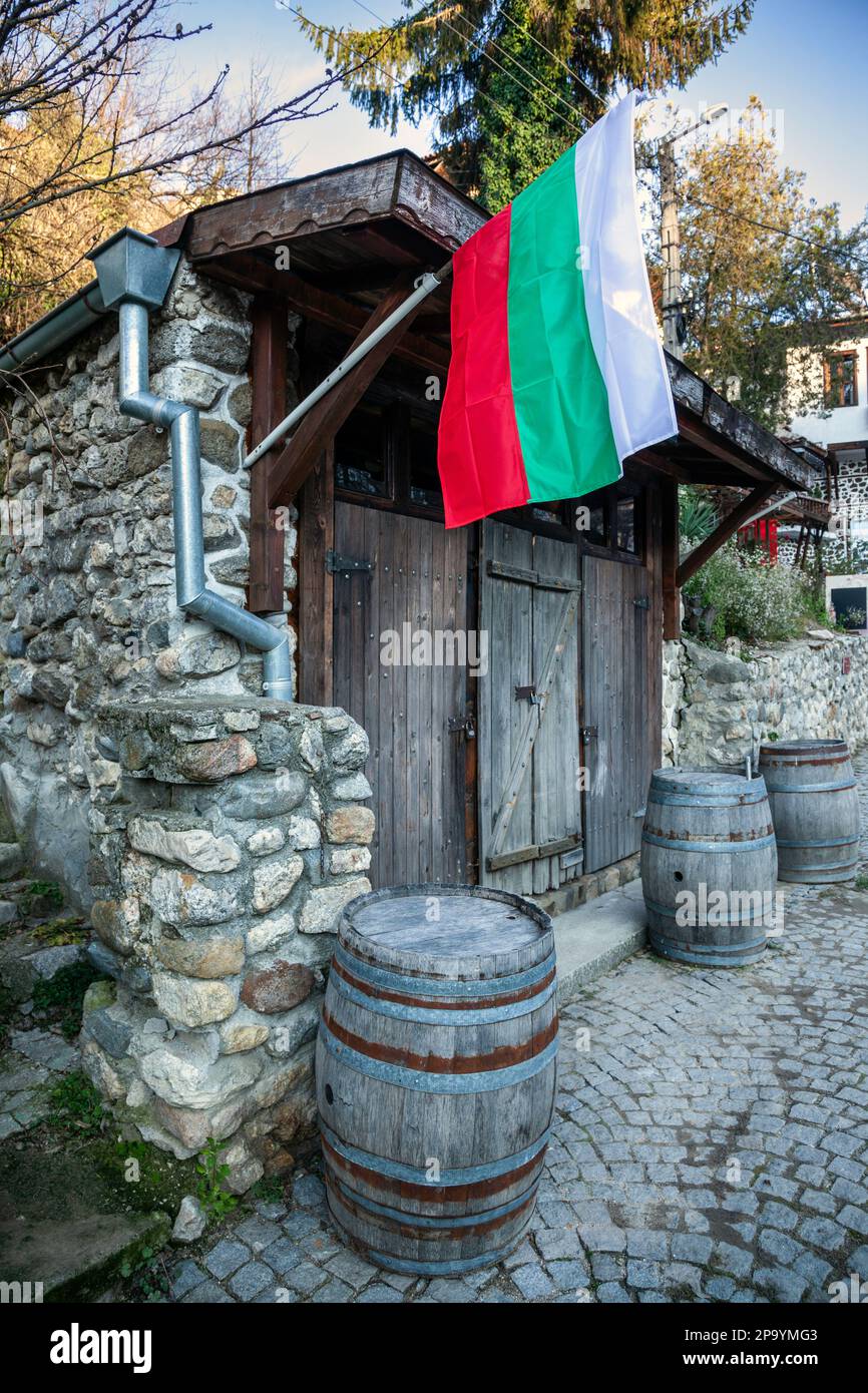 Old warehouse of a local winery in Melnik, Bulgaria, with wooden barrels and the bulgarian flag hanging from a post. Stock Photo