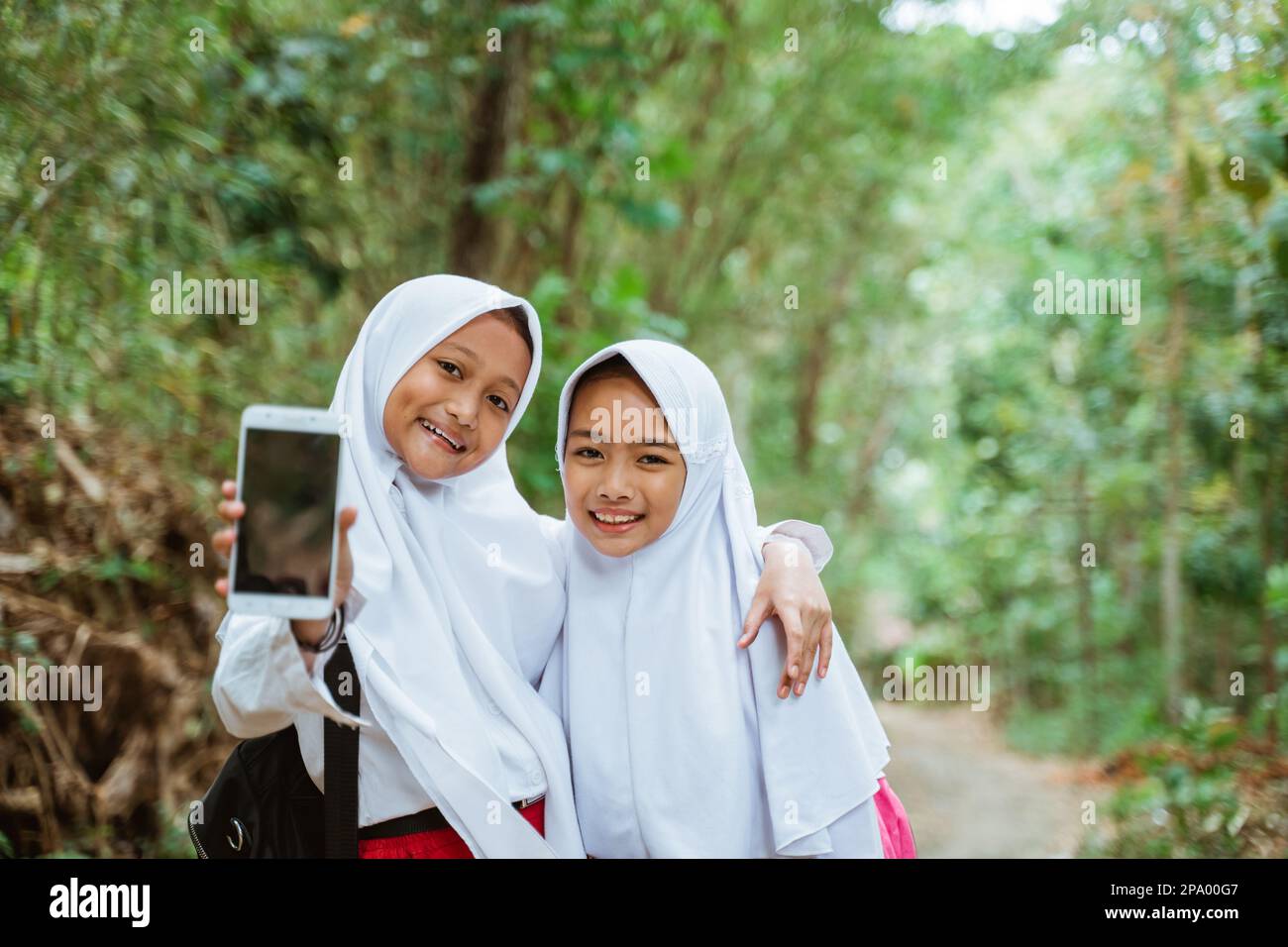 two female elementary students standing together showing the phone to the camera Stock Photo
