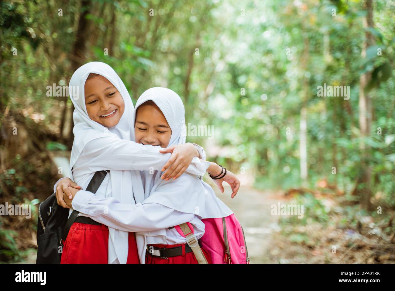 two beautiful elementary students standing together and hugging each other Stock Photo