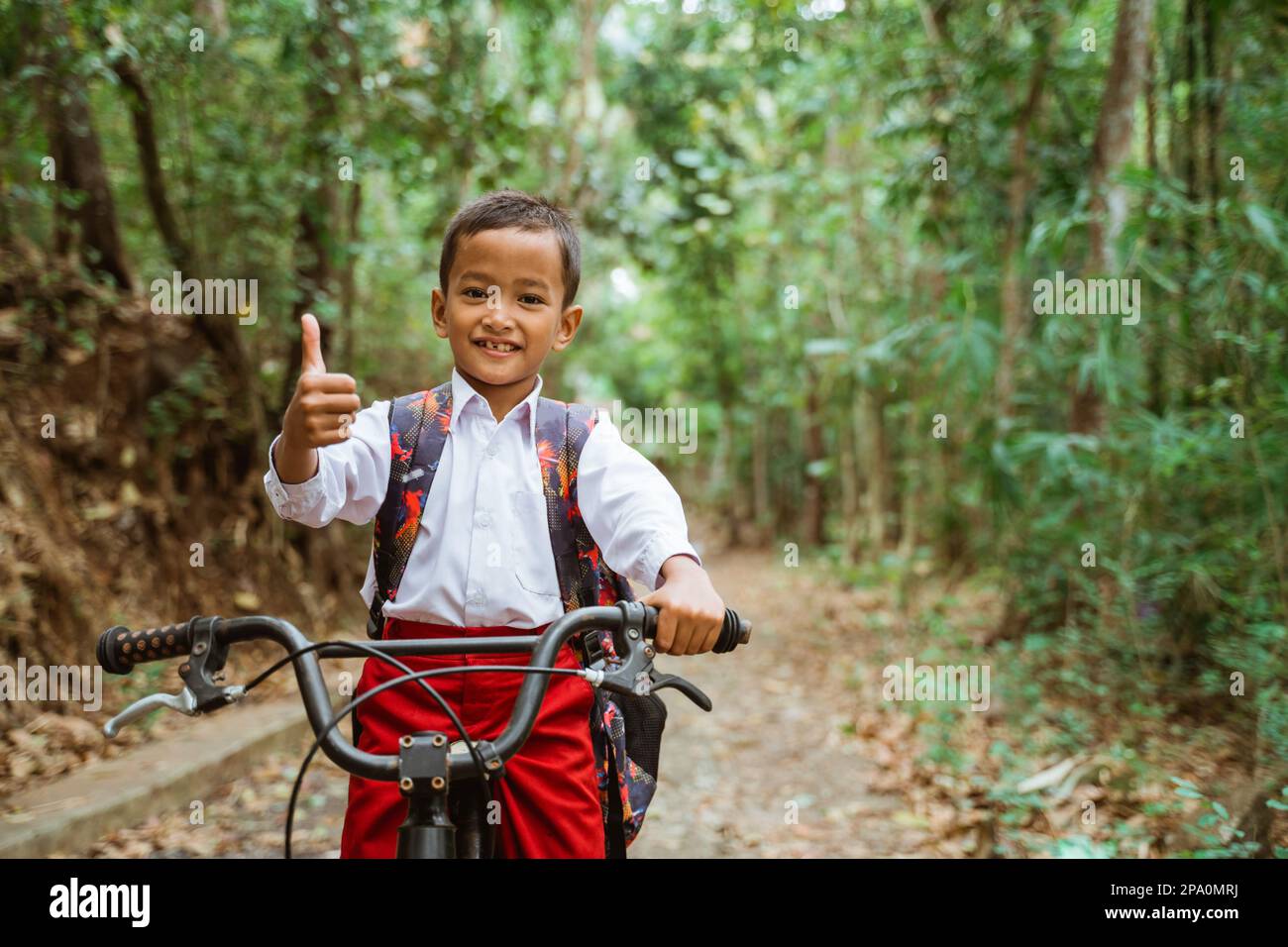 a male elementary student in uniform riding his bike with thumb up Stock Photo