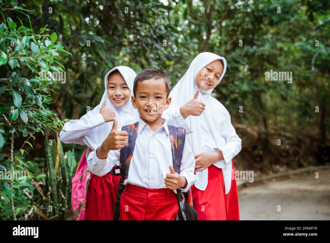 three elementary students standing at the side of country road with thumbs up Stock Photo