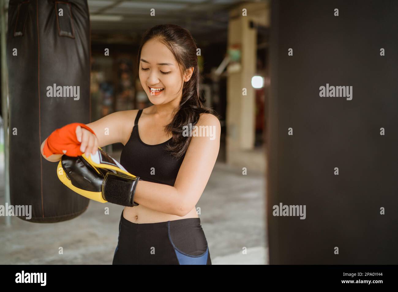 a boxer wearing the boxing gloves while standing around the heavy bags Stock Photo