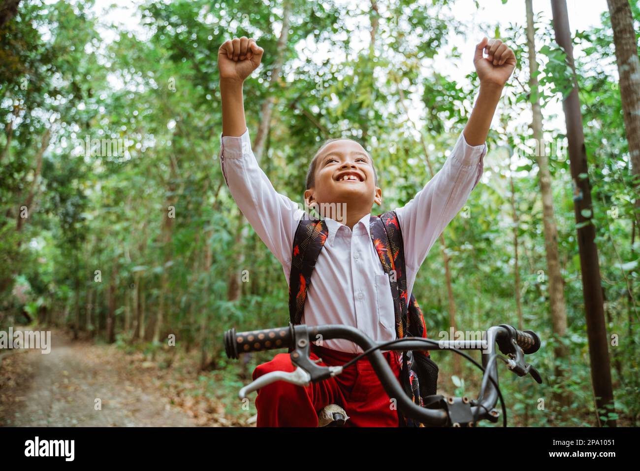 a male elementary student riding his bike and raised his hands Stock Photo