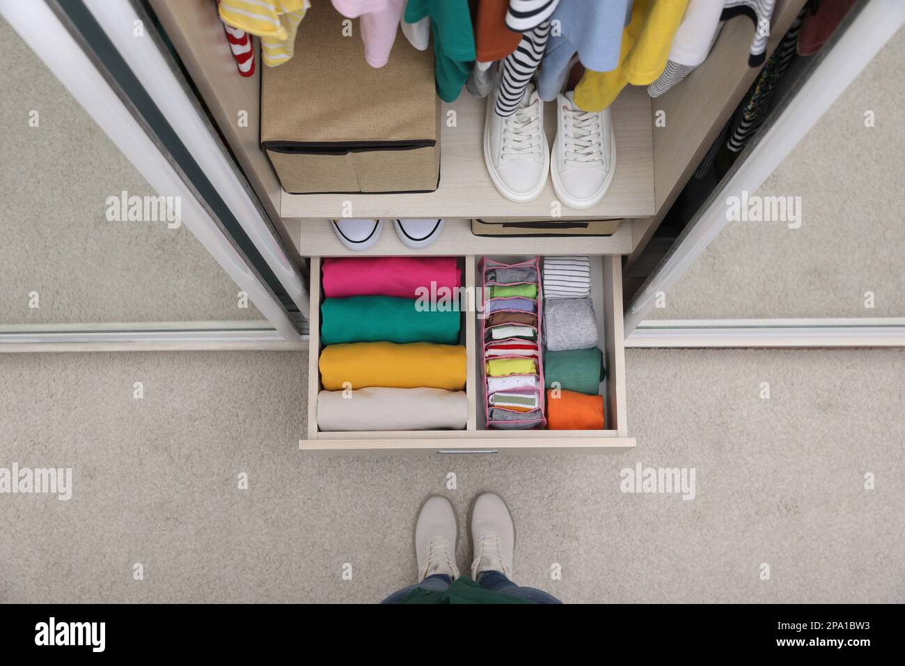 Woman near wardrobe with organized clothes and shoes indoors, top view