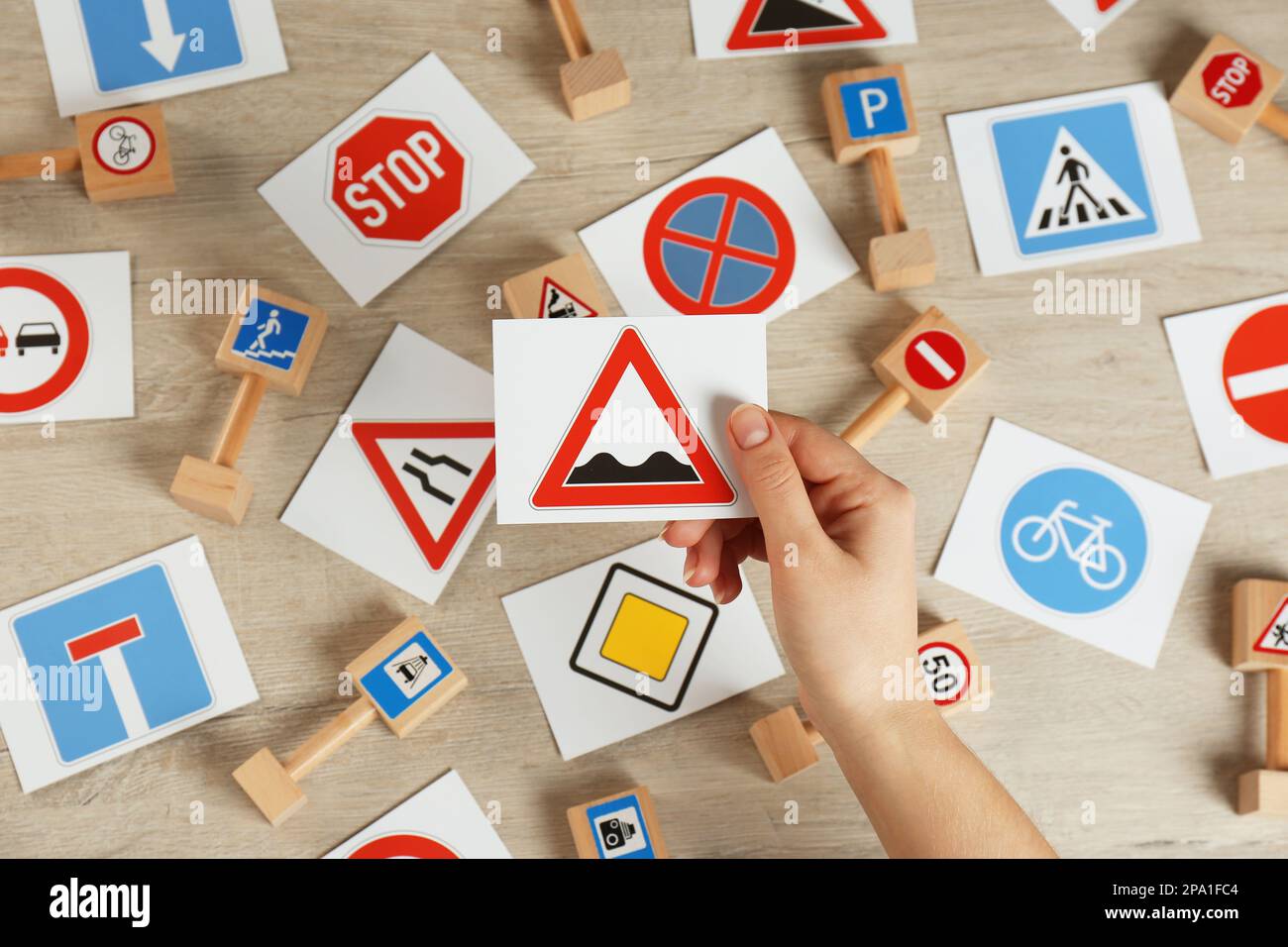 Woman holding rough road sign over wooden table, top view. Driving license exam Stock Photo