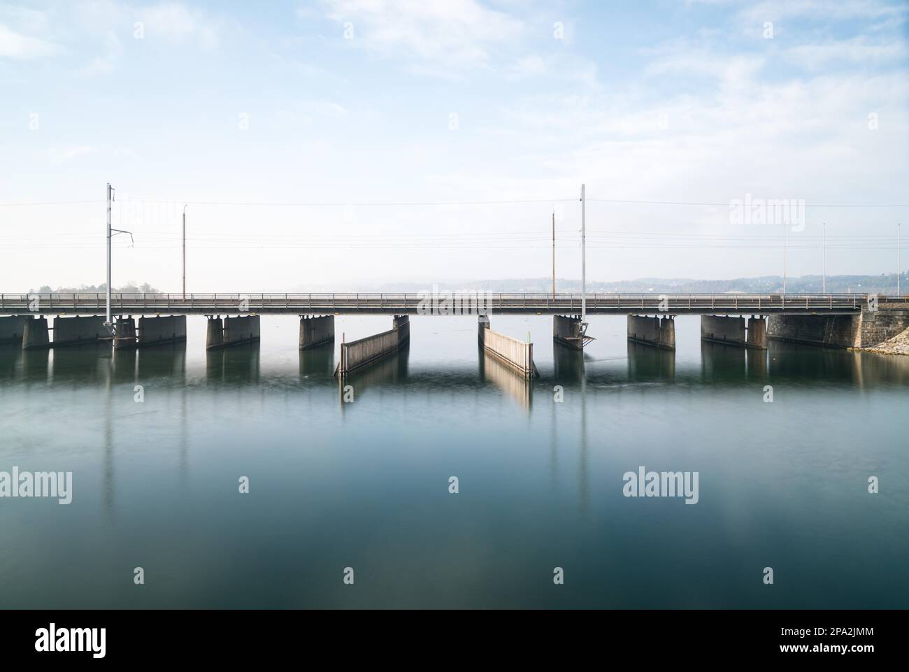 A concrete bridge over water with a train line and road running parallel and a boat and ship passageway below on the Lake of Zurich near Rapperswil Stock Photo