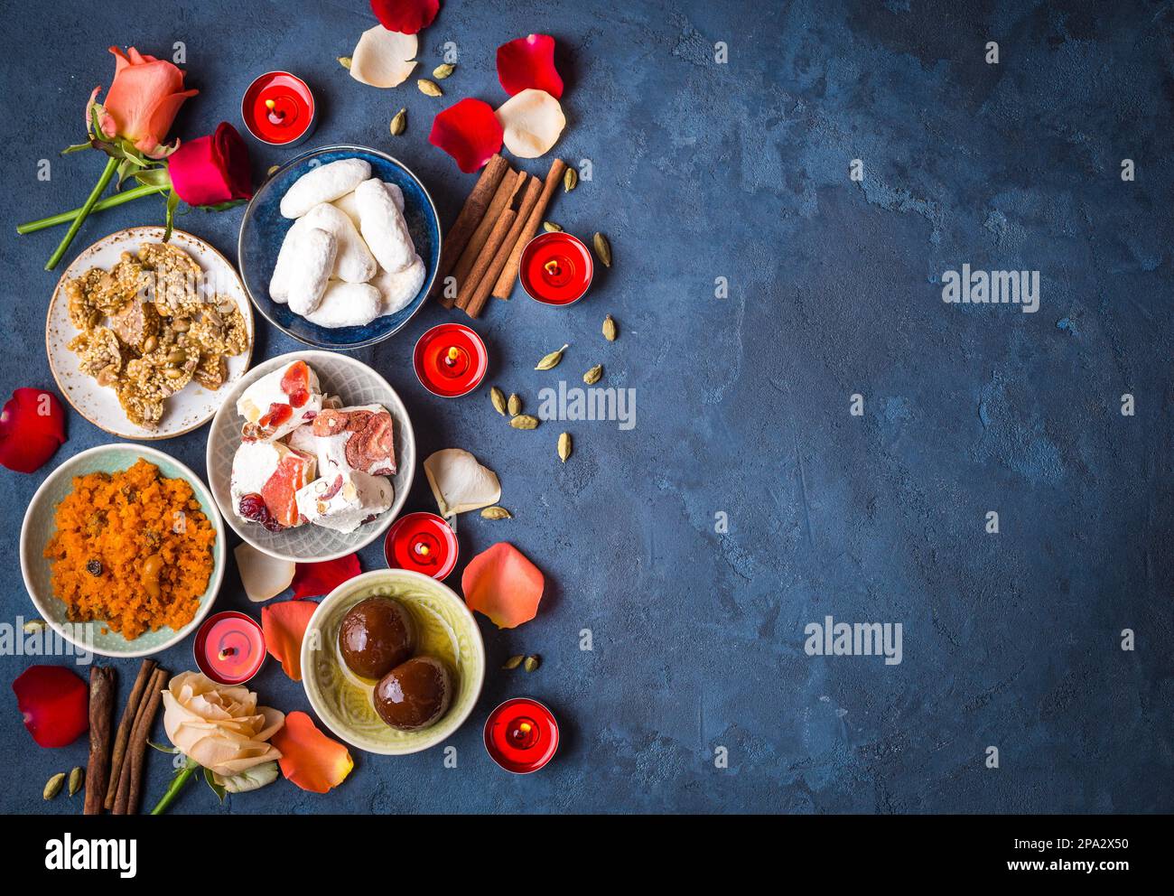 Indian Diwali celebratory background with traditional sweets. Gulab jamun, carrot halwa, snacks with candles, flowers. Assorted indian desserts. Stock Photo