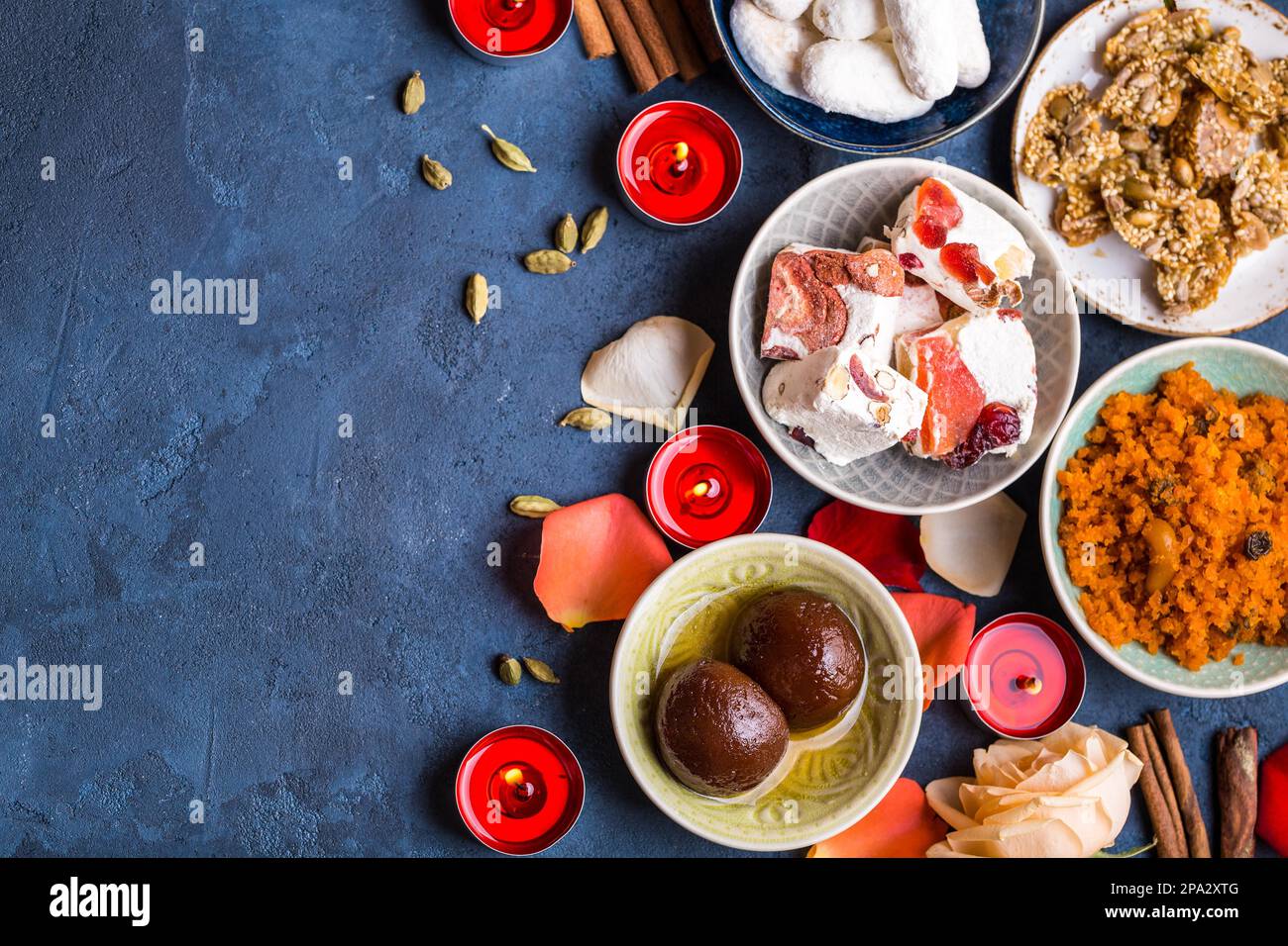 Indian Diwali celebratory background with traditional sweets. Gulab jamun, carrot halwa, snacks with candles, flowers. Assorted indian desserts. Stock Photo