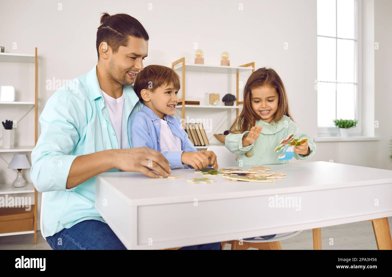 Father playing with his two kids in a puzzle in the living room at home. Stock Photo