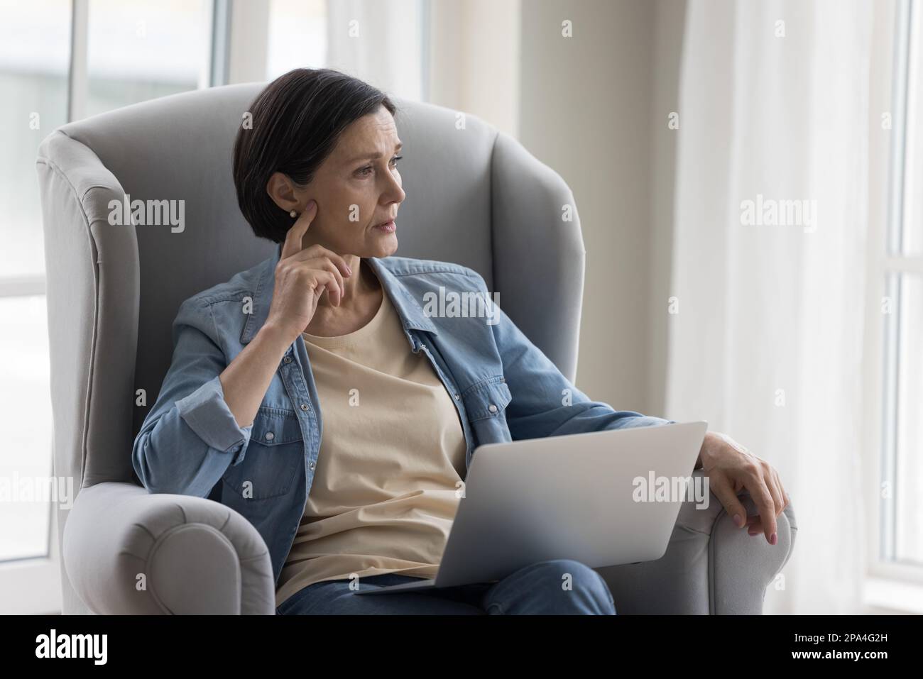 Thoughtful mature woman sitting in armchair at home Stock Photo - Alamy