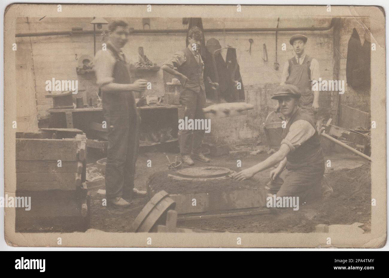 Photograph of early 20th century foundry or workshop, with men standing around a mould for casting metal Stock Photo