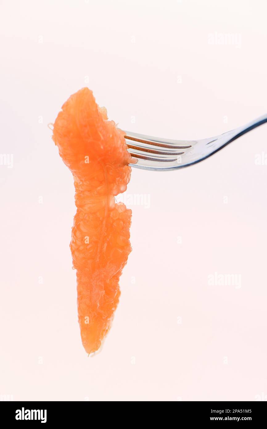 A single segment of grapefruit on a fork for ready to eat against a