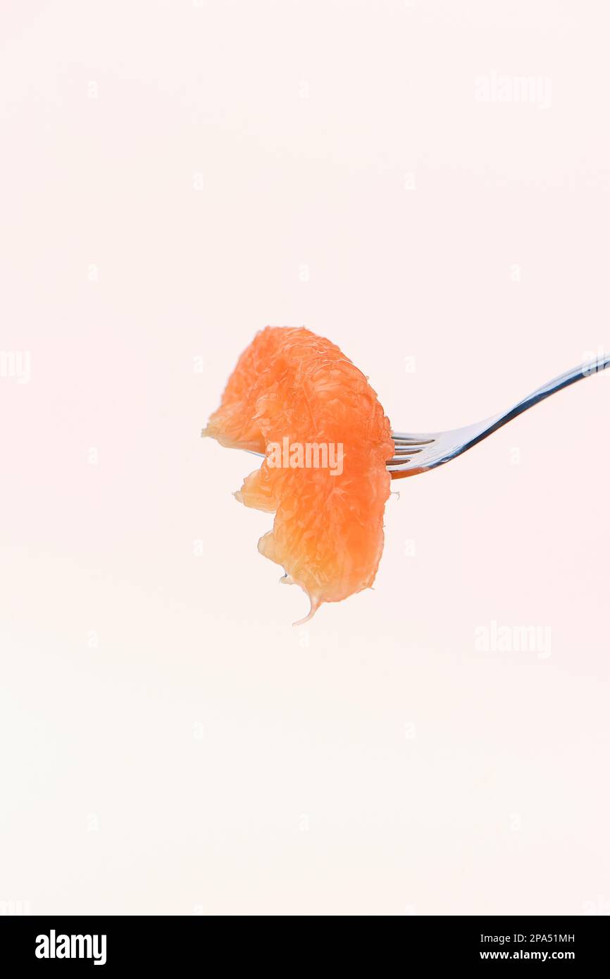 A single segment of grapefruit on a fork for ready to eat against a