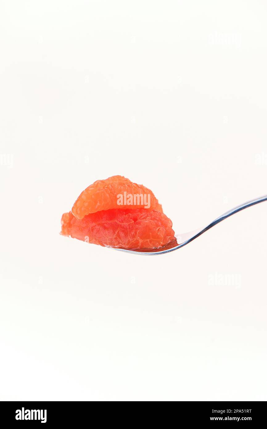 A single segment of grapefruit on a fork for ready to eat against a