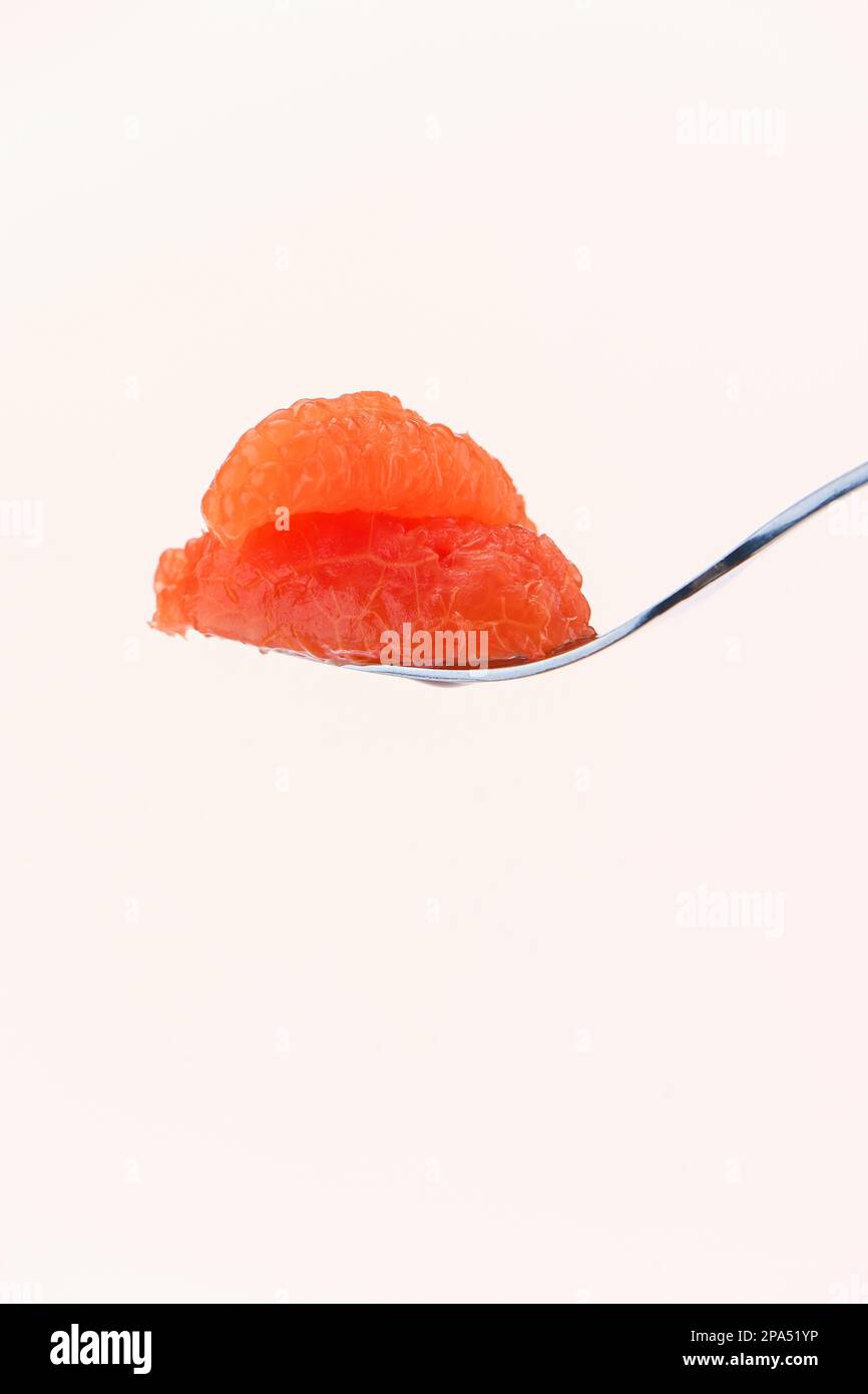 A single segment of grapefruit on a fork for ready to eat against a