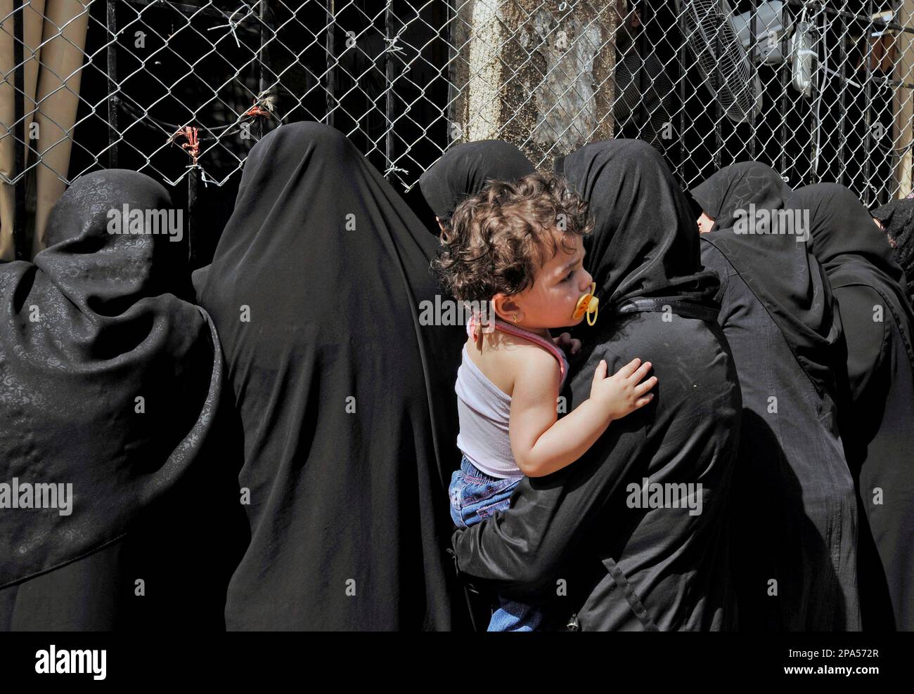 Shiite Lebanese women in black dress look through a fence to follow the  funeral procession of Mohammad Ali Mourtada, a Hezbollah fighter who was  kidnapped and killed on Saturday in a Southern