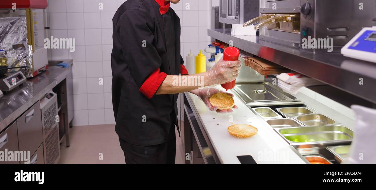 Cook adding a ketchup on burger. Preparing burger in restaurant. Hands