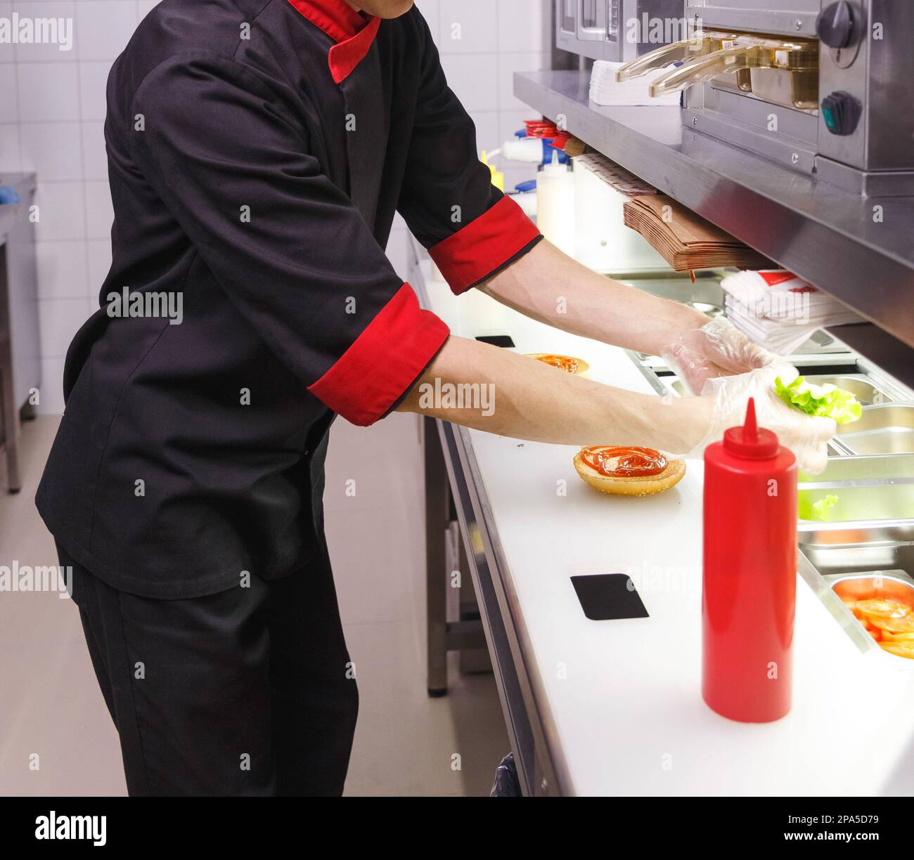 Cook adding a ketchup on burger. Preparing burger in restaurant. Hands