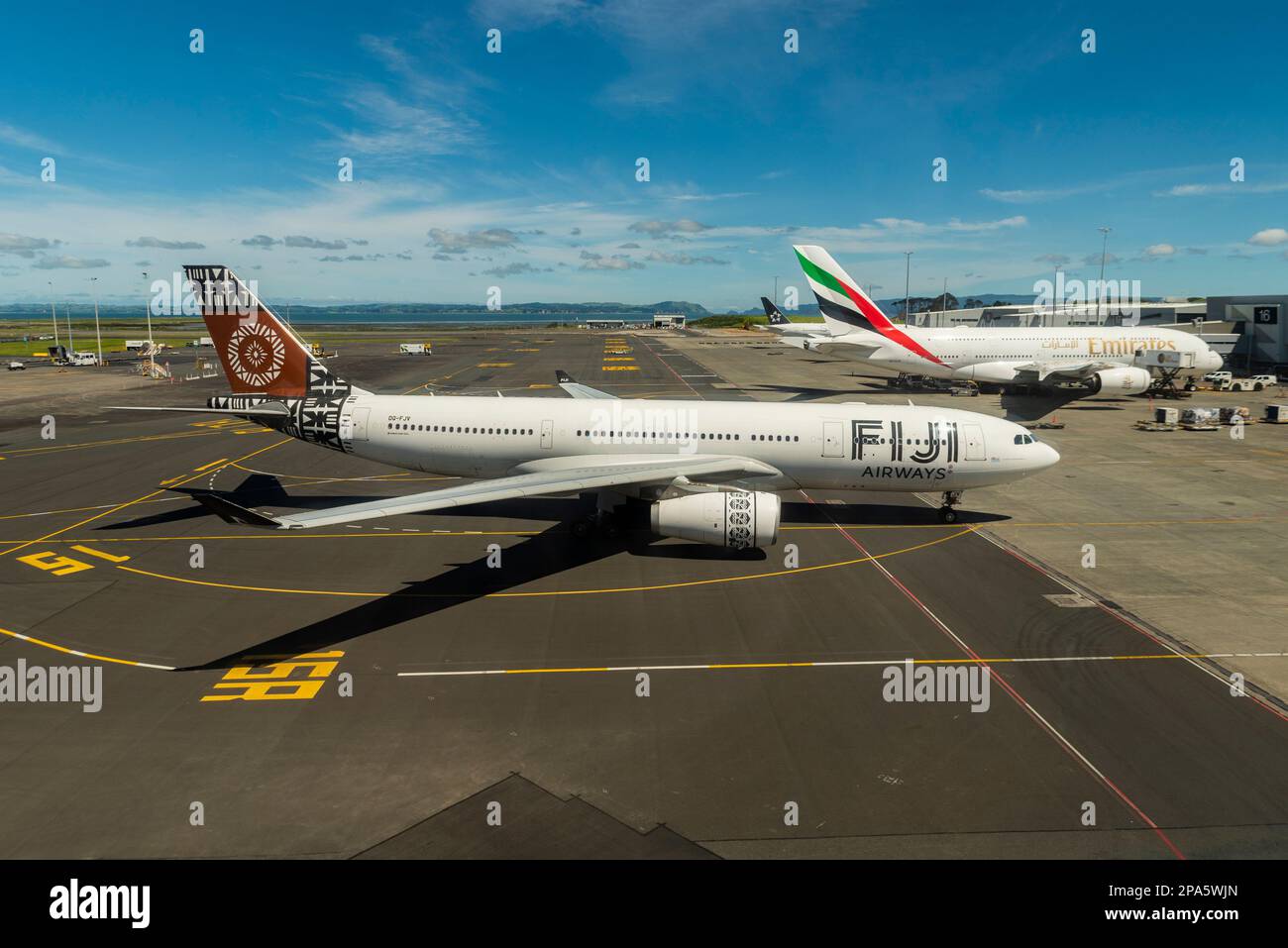 Fiji Airways Airbus A330 airliner jet plane DQ-FJV taxiing to stand at Auckland Airport, New Zealand, by Emirates A380 A6-EVR. Air travel in Pacific Stock Photo