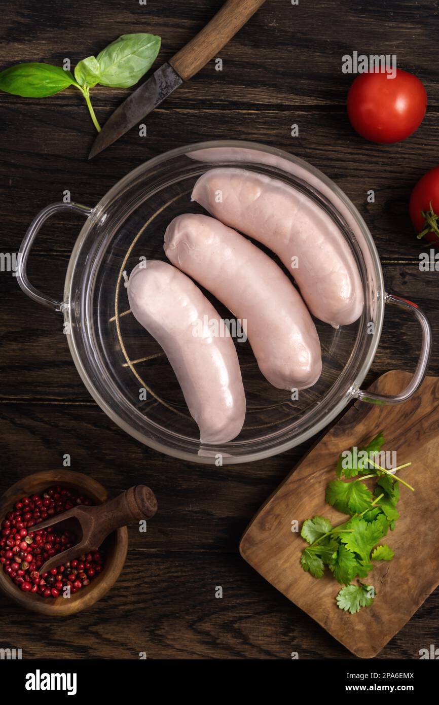 Three white sausages in a glass saucepan and spices, top view Stock Photo