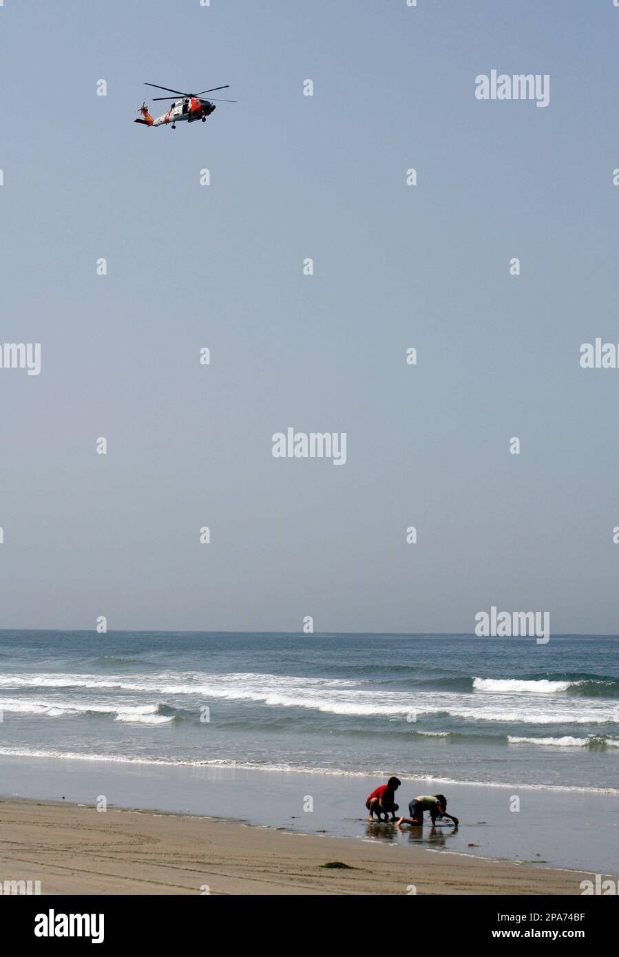 Children play on the beach as a U.S. Coast Guard helicopter flies above
