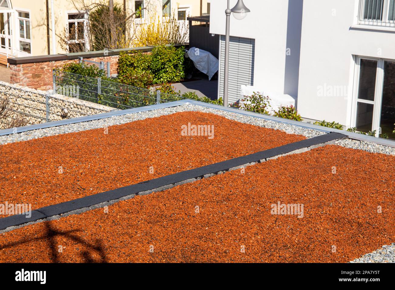 Flat roof with pebbles and red decorative stones, on which planting is