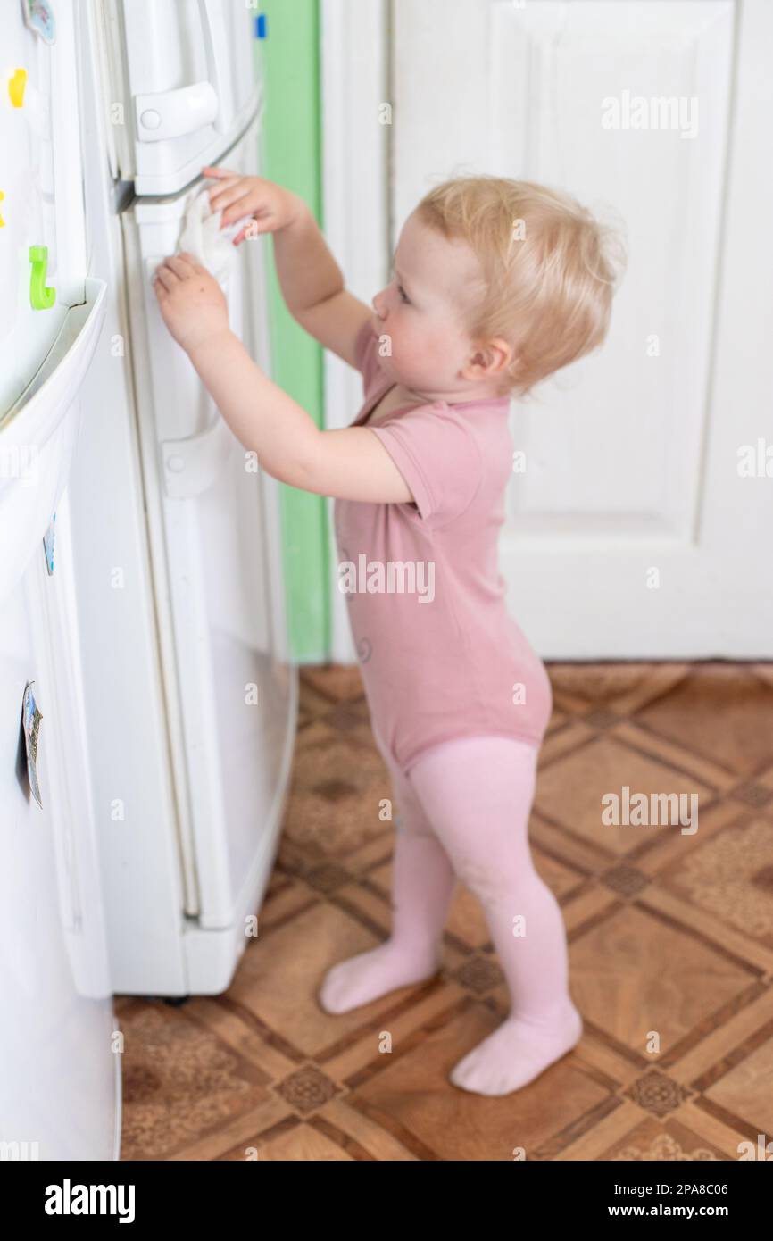A toddler washes the refrigerator with wet wipe tissue during a viral epidemic. Cleaning home. Teaching children to be independent. use of wet wipes Stock Photo