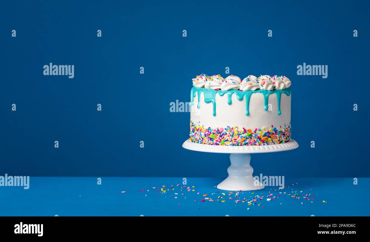 White Birthday drip cake with teal ganache and colorful sprinkles over a dark blue background. Simple and trendy. Copy space. Stock Photo