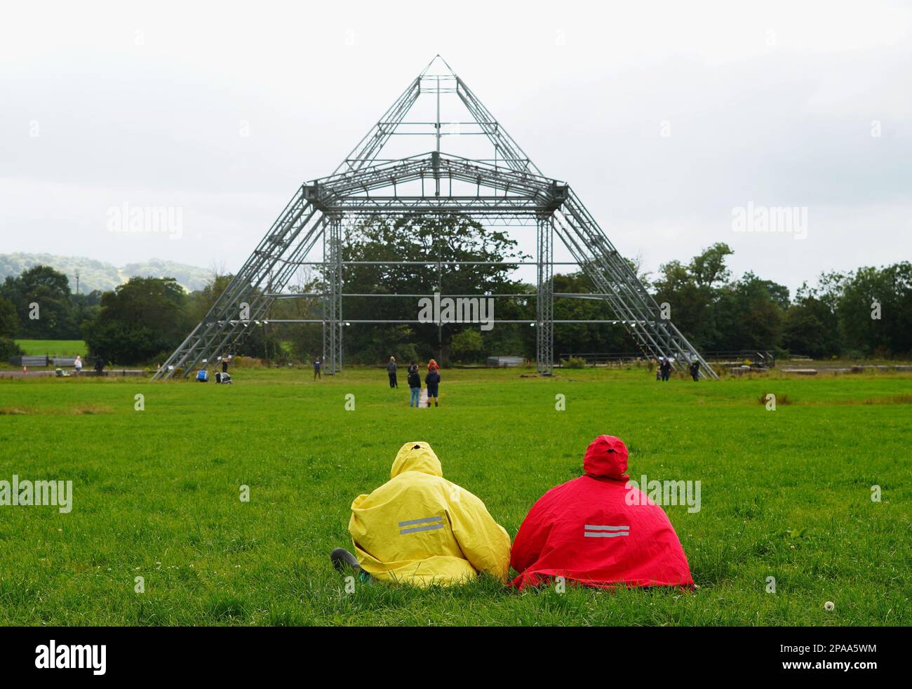 A couple in colourful raincoats, enjoy the view of the empty Pyramid Stage at Worthy Farm, Pilton, home of Glastonbury Festival. Stock Photo