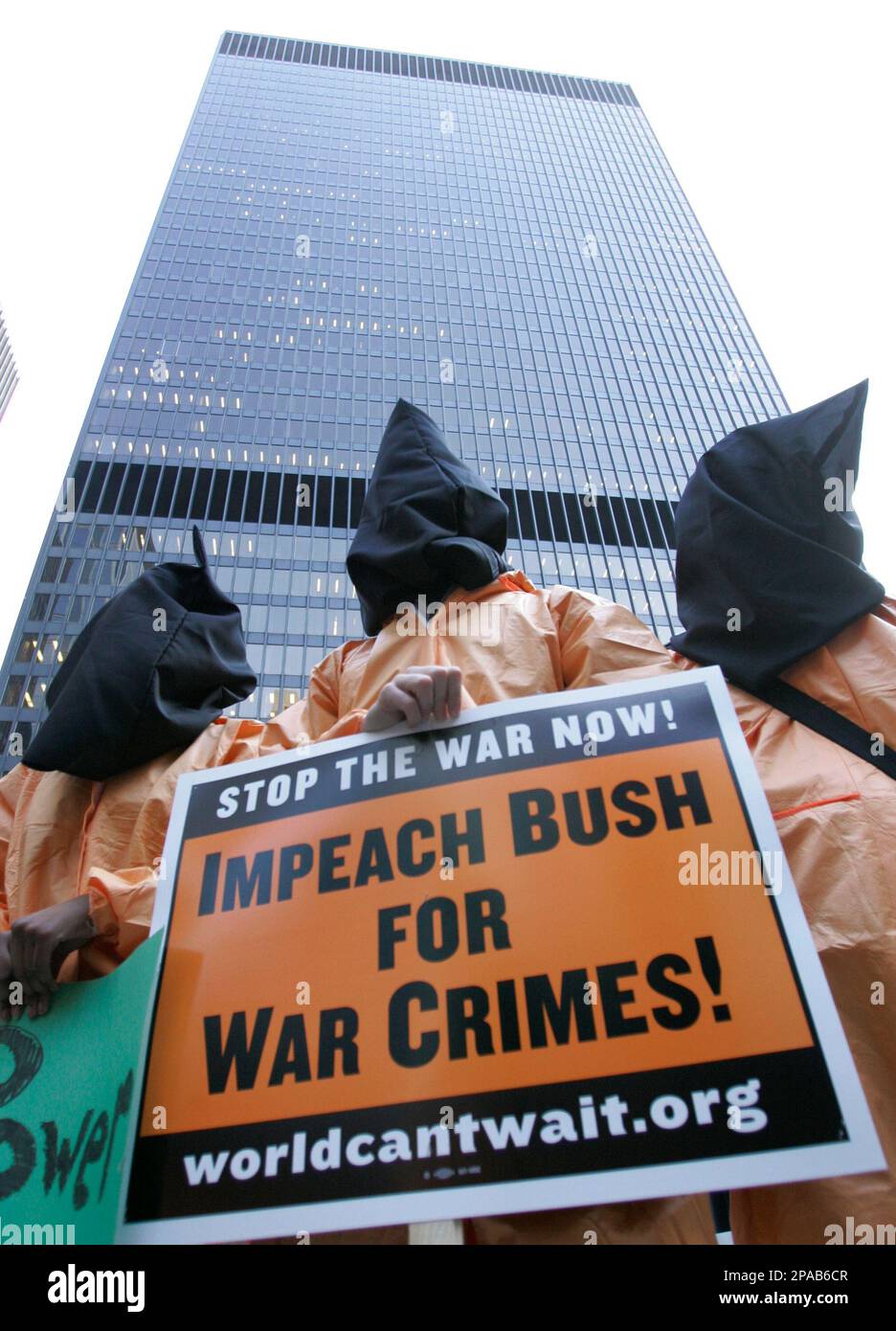 Three people wearing hoods and orange jump suits participate in an anti ...