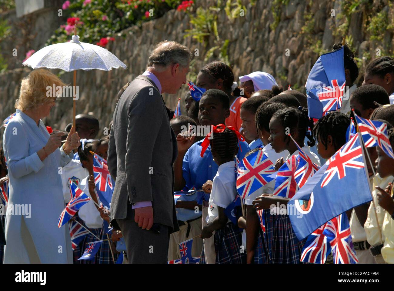 Britain's Prince Charles, center, speaks to school children upon their arrival to Little Bay, in the Caribbean island of Montserrat, Saturday, March 8, 2008, accompanied by his wife Camilla, the Duchess of Cornwall, left. Both toured the area that was devastated by the eruption of the Soufriere Hills volcano a decade ago, as part of a five-island Caribbean tour. (AP Photo/Wayne Fenton) Stock Photo