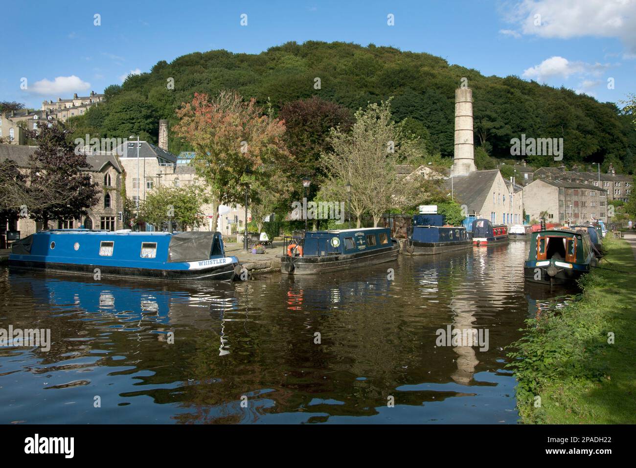 narrowboats on the Rochdale Canal at Hebden Bridge with the former chimney of Crossley Mill in the distance, West Yorkshire Stock Photo