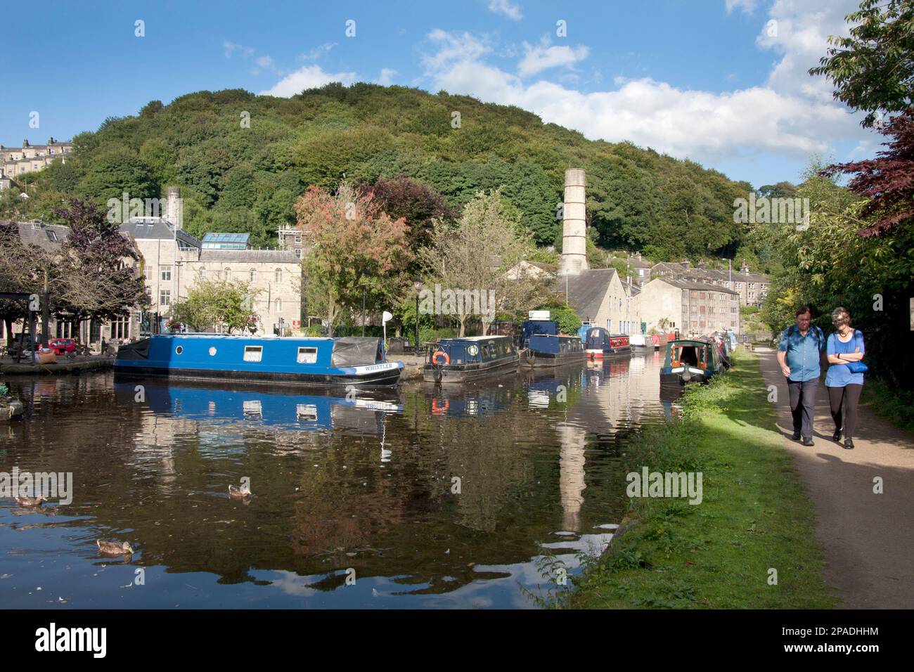narrowboats on the Rochdale Canal at Hebden Bridge with the former chimney of Crossley Mill in the distance, West Yorkshire Stock Photo