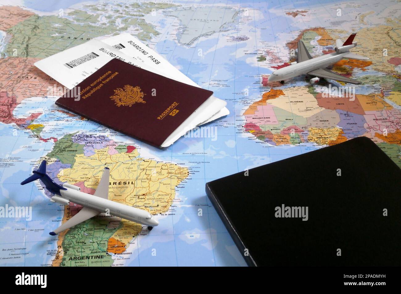 World map with on it, two toy planes, a closed black note pad and a French passport with 2 plane tickets inside. Stock Photo