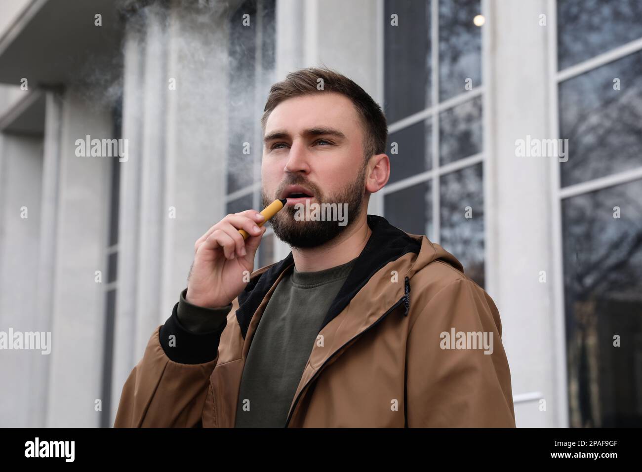 Handsome young man using disposable electronic cigarette outdoors Stock Photo
