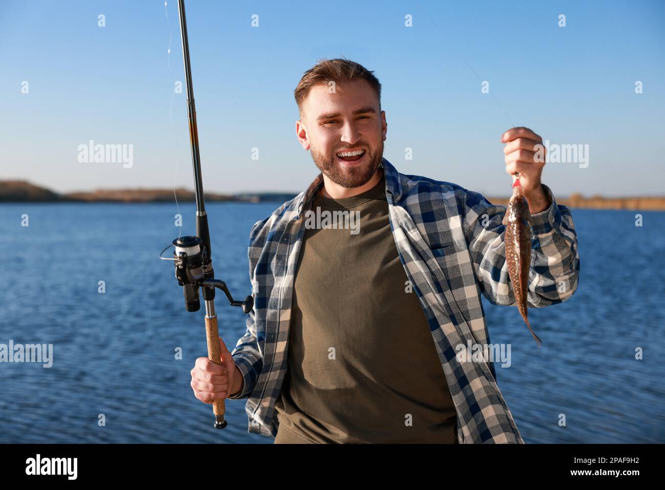 Fisherman holding fishing rod and catch at riverside Stock Photo