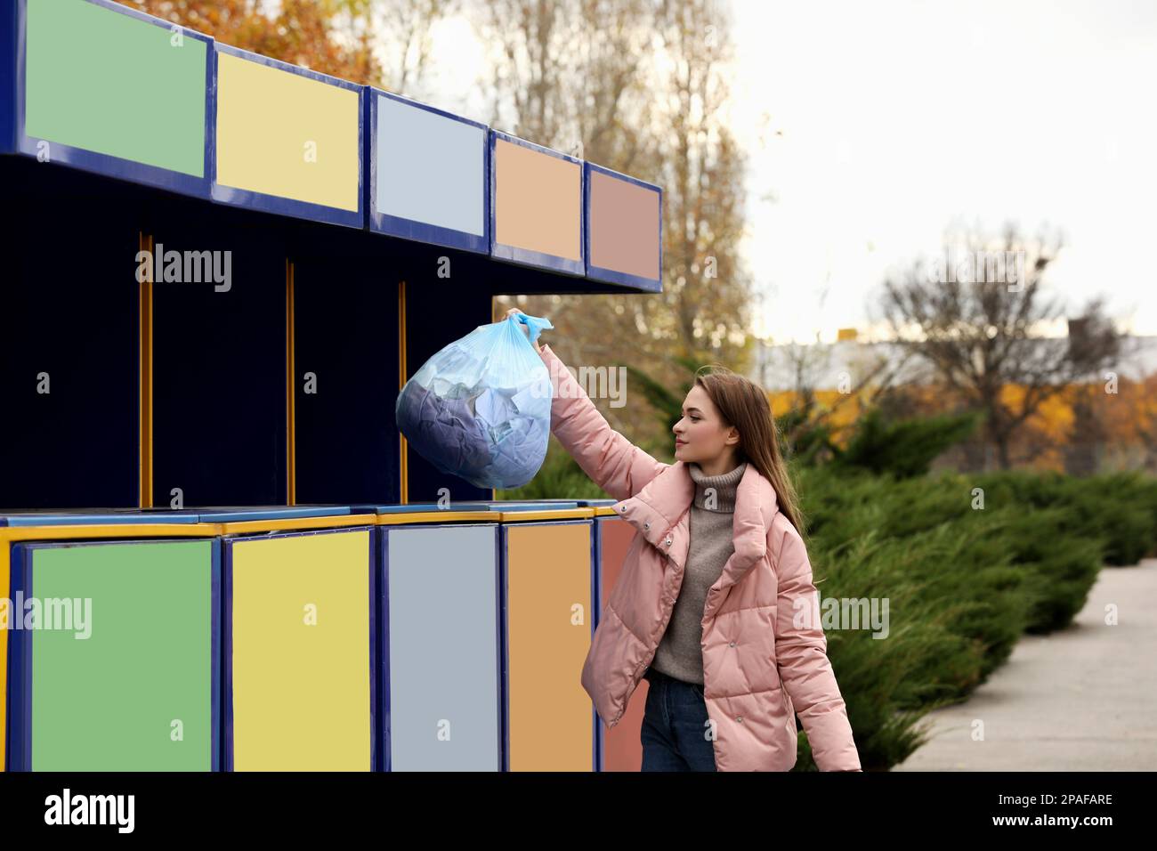 Woman throwing garbage into bin at recycling point outdoors Stock Photo