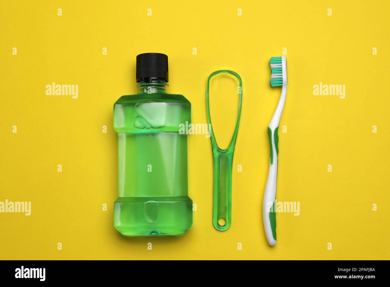 Tongue cleaner, mouthwash and toothbrush on yellow background, flat lay