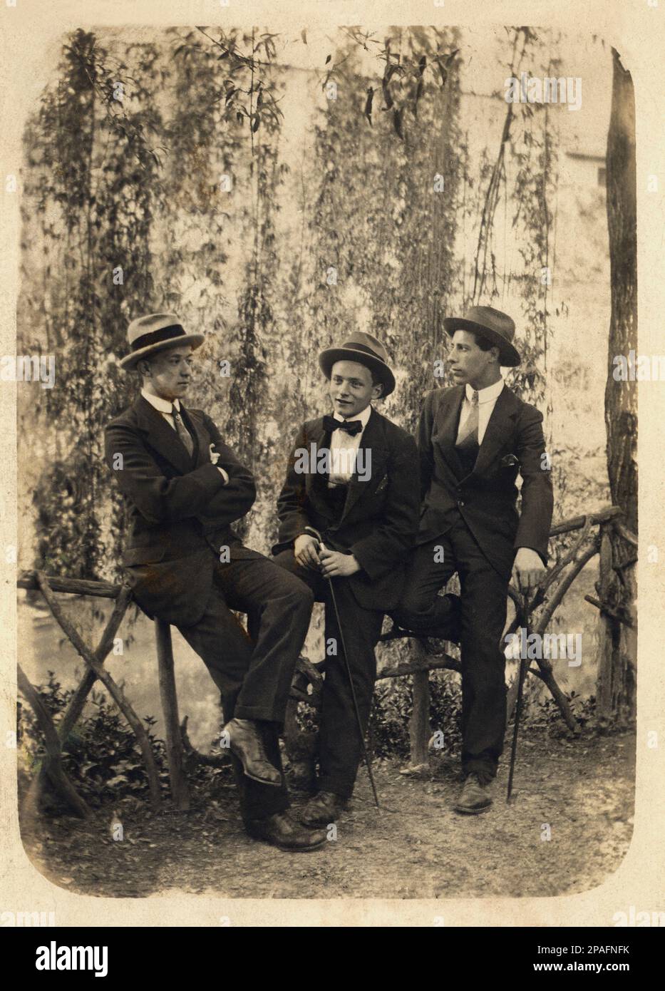 1920 ca , Milano , Italy  : Three friends in a pubblic park  ( with probability at Parco del Castello Sforzesco ) -   - FOTO STORICHE - HISTORY PHOTOS -   - ITALY - ITALIA - hat - cappello -  AMICO - AMICI - CAPPELLO - HAT - FASHION - MODA - cravatta - tie - bastone da passeggio - cane - papillon - tie bow  - XX CENTURY - NOVECENTO - passeggiata - walk - stroll - parco pubblico - giovanotto - giovanotti - young man - men  - uomo - uomini - domenica pomeriggio - sunday afternoon - garedn - giardino  ----      ARCHIVIO GBB Stock Photo