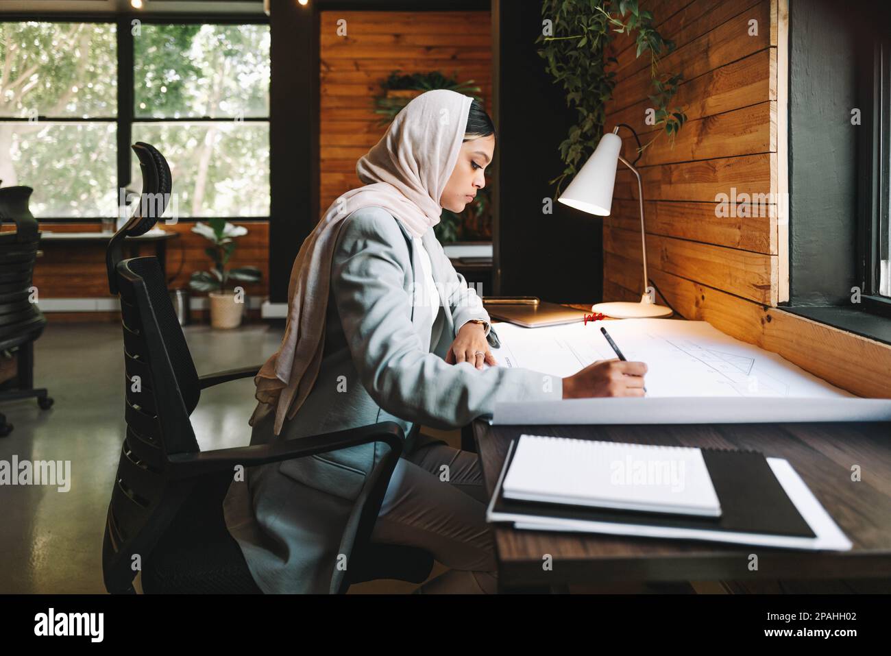 Muslim designer working on architectural blueprints in a modern office. Innovative young businesswoman planning a new creative project. Female archite Stock Photo