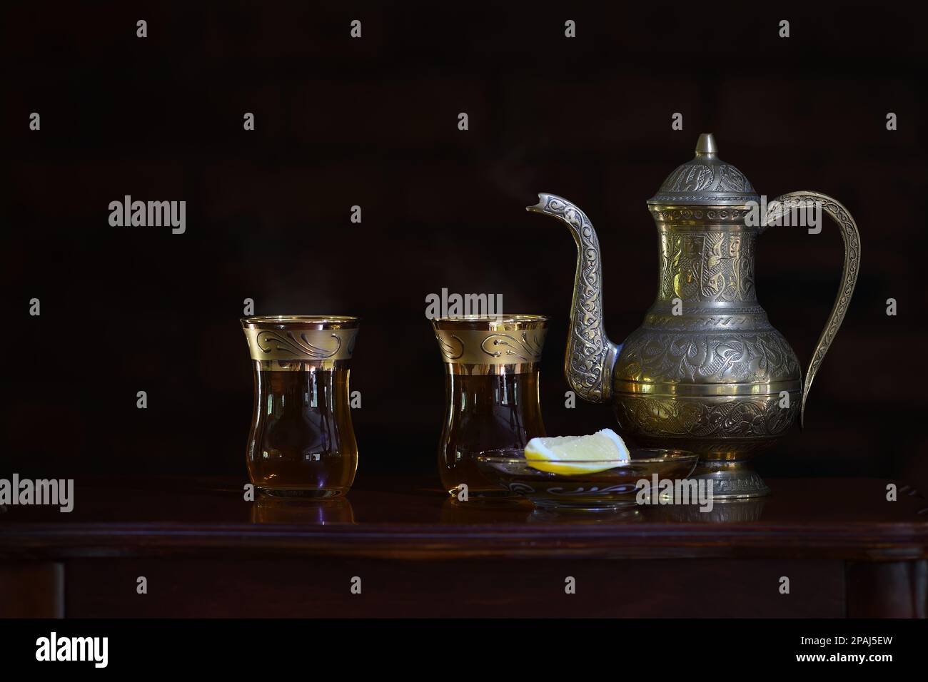 A classic, celebratory, ornate Turkish teapot and glasses shining in soft dark mood lighting with copy space to the left Stock Photo