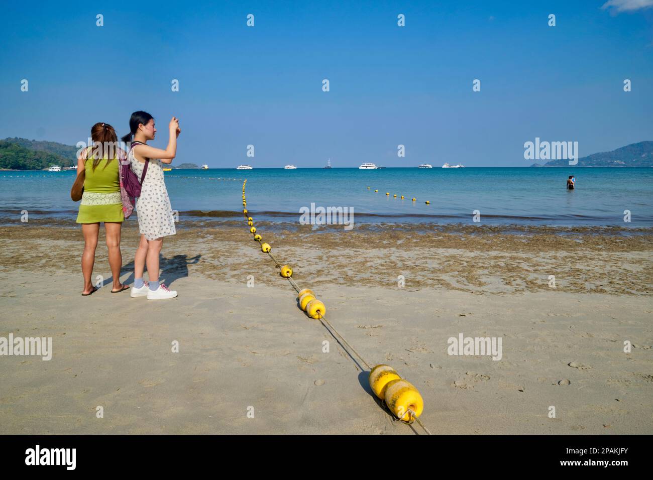 Two young female Thai tourists taking photos at Patong Beach, Phuket, Thailand Stock Photo