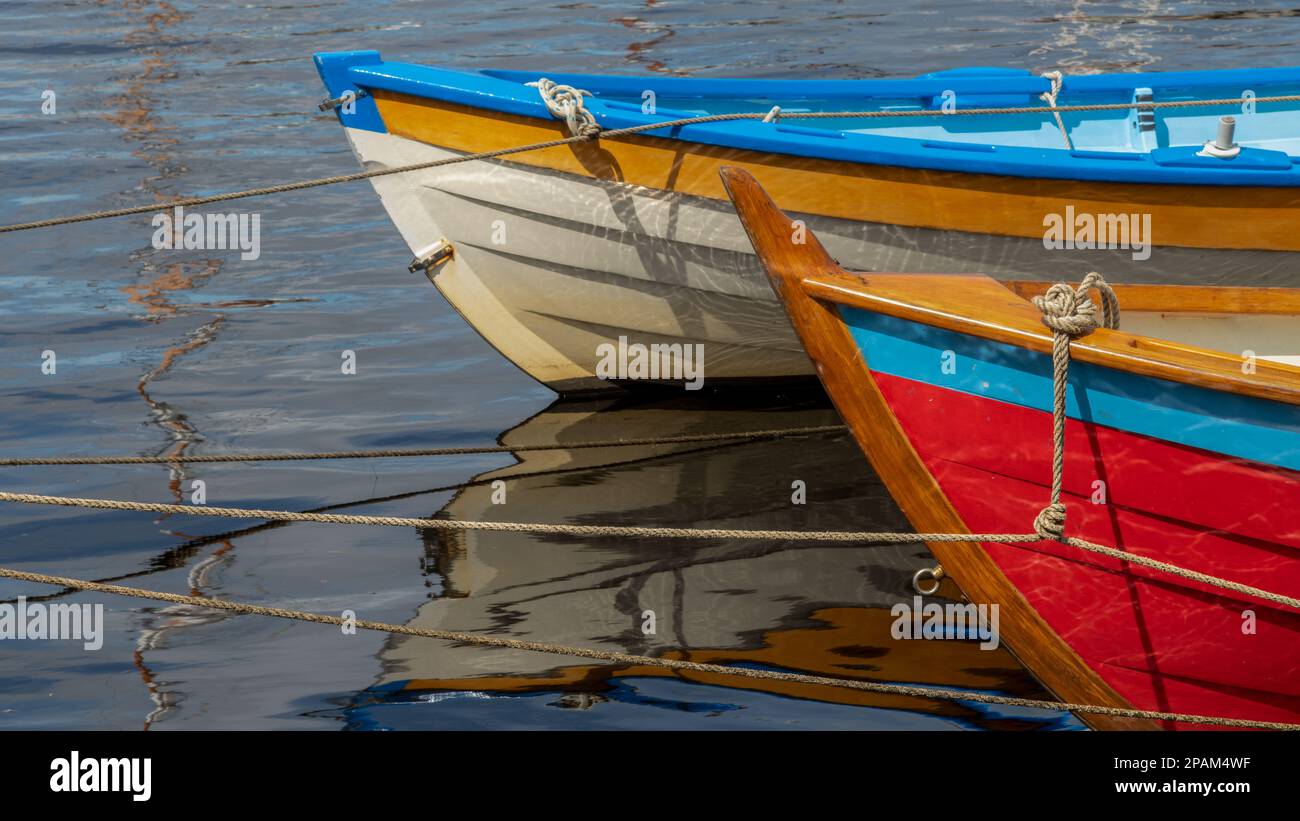 Abstract of two colourful clinker built boats with reflections and tied to a mooring with ropes. Stock Photo