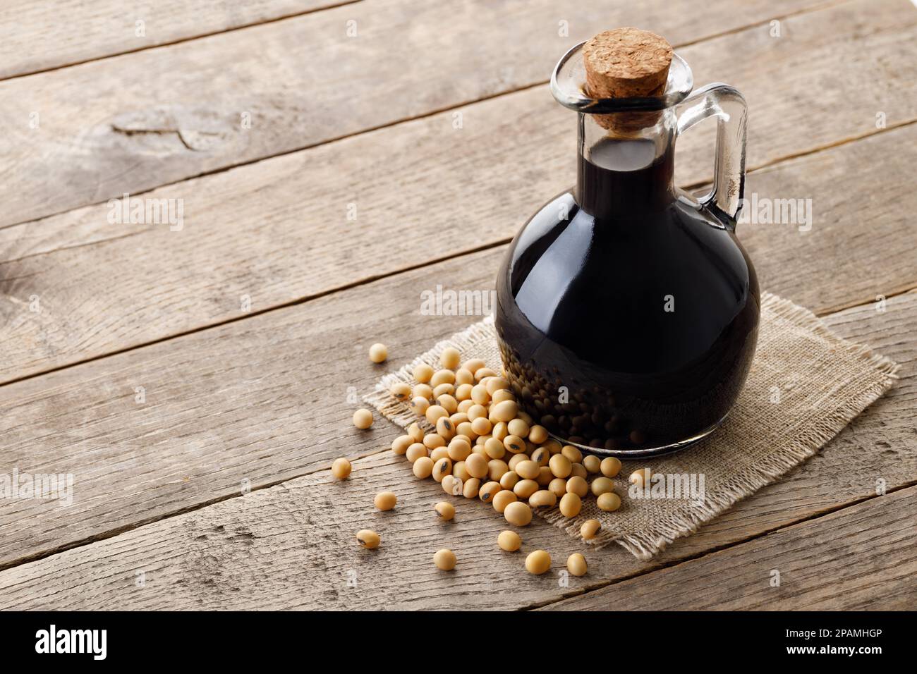 soy sauce in glass bottle with dry soybeans on wooden table Stock Photo