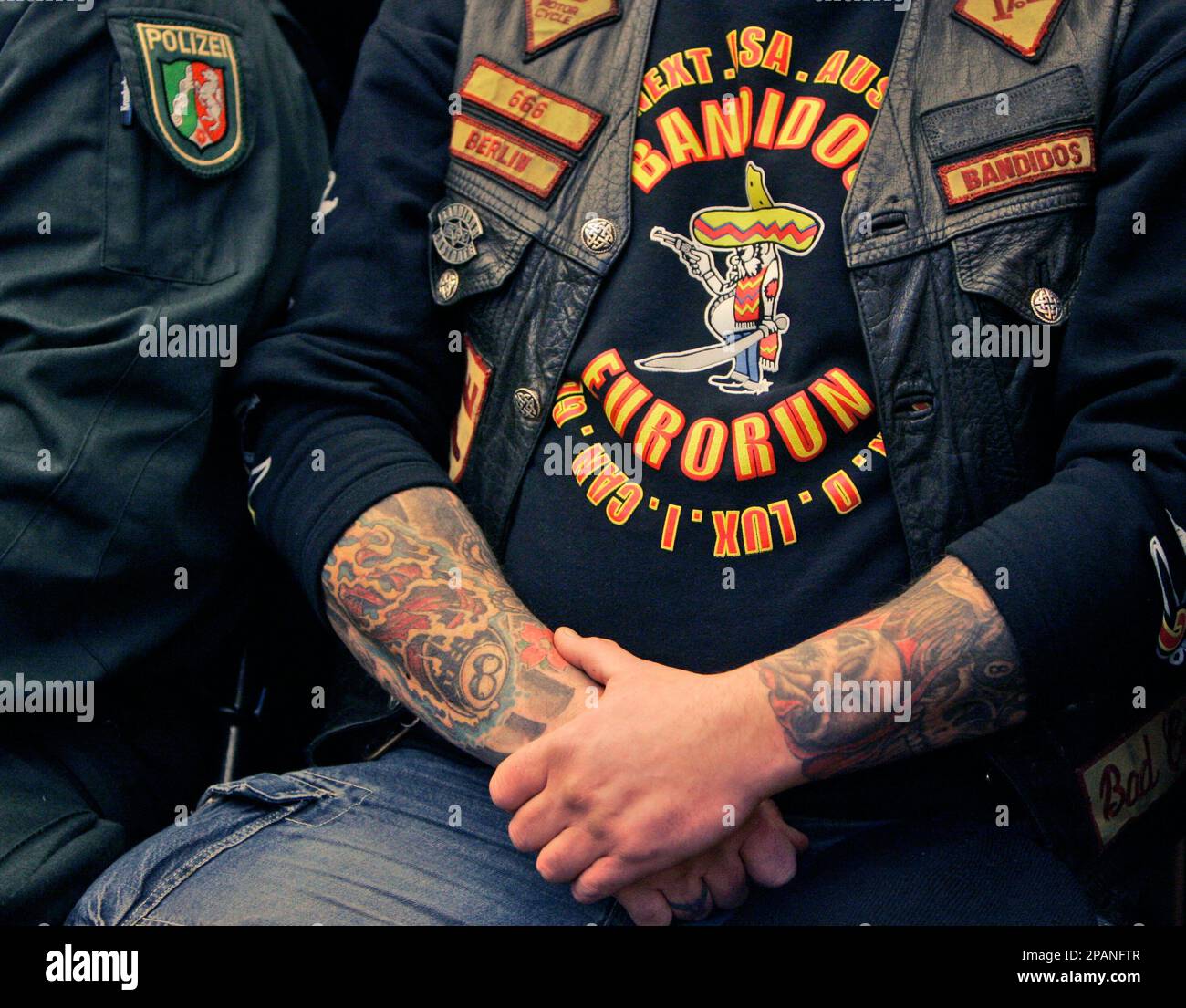 A member of the Bandidos gang sits beside a police officer inside the ...