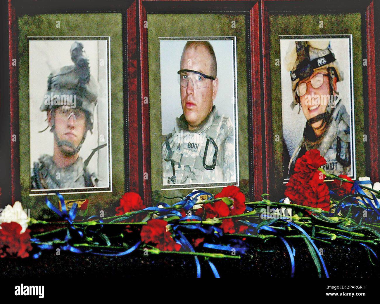 Flowers left by mourners lie at the base of photos of, from left ...