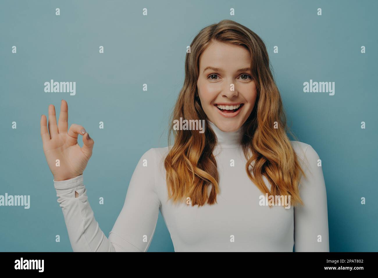 Half-length image of beautiful excited joyful young lady with dyed light-brown hair gesturing ok symbol with fingers, looking at camera with beaming s Stock Photo