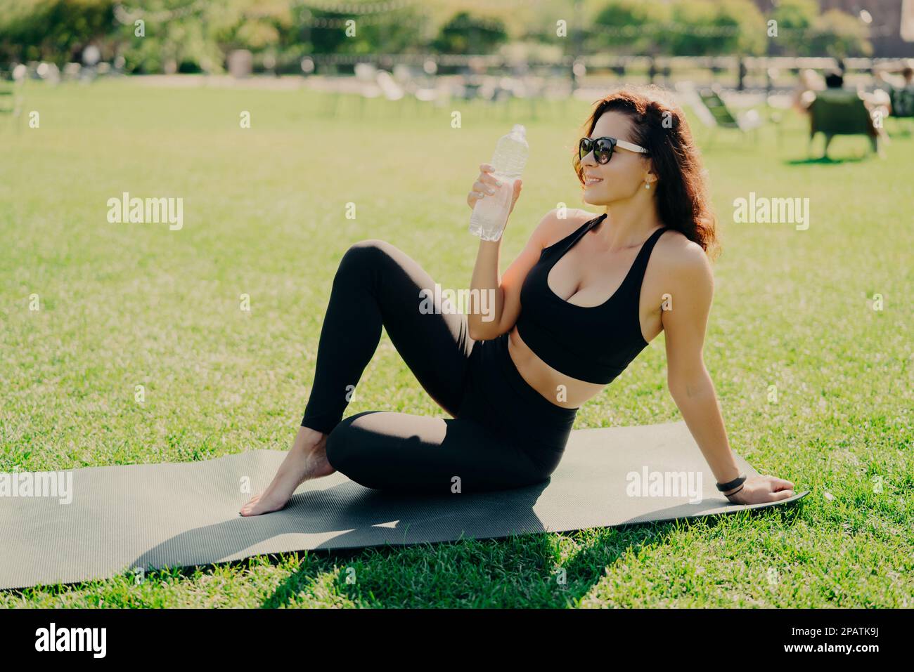 Outdoor shot of active slim woman drinks water from bottle feels thirsty after fitness training concentrated into distance wears cropped top and leggi Stock Photo